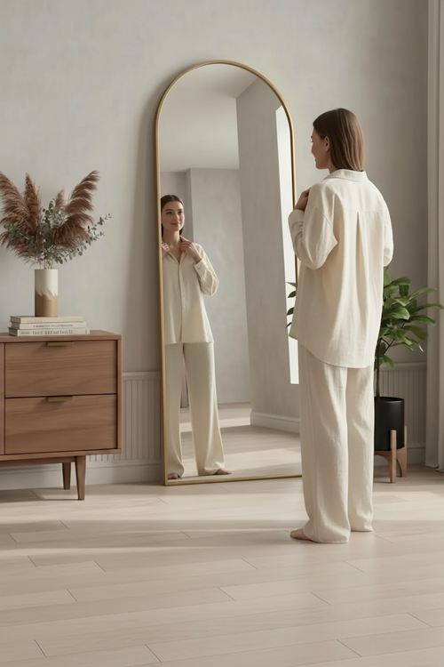 Woman in cream outfit checking reflection in gold arch floor mirror